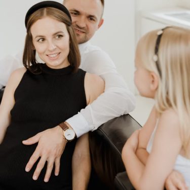 A pregnant woman sits with her family on a sofa, capturing a warm moment of togetherness.